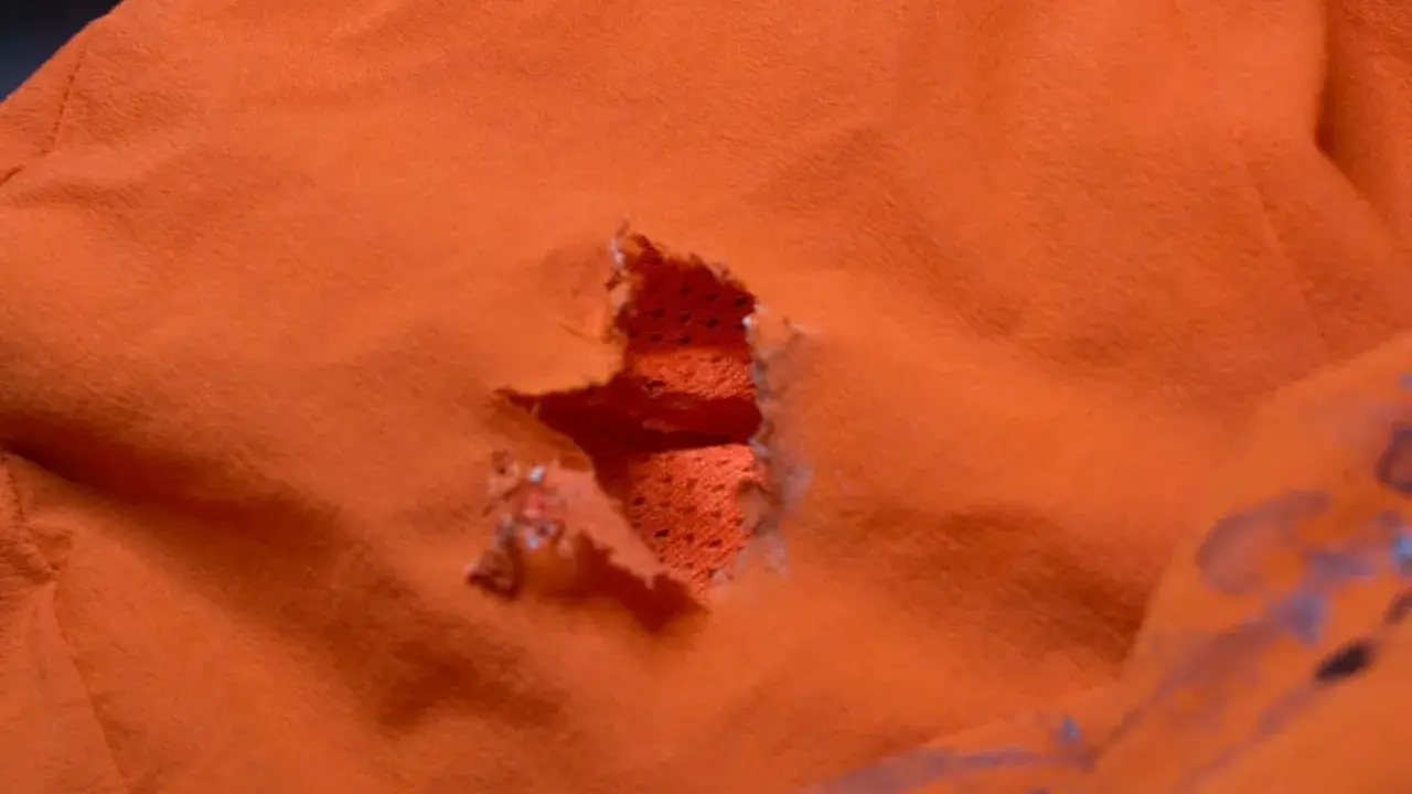 Ein Loch in einer orangefarbenen Polyesterjacke, bereit für einen Flicken.