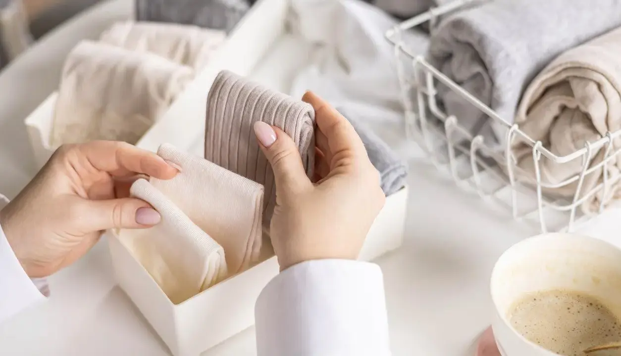 Hände sortieren gefaltete Socken in einer Schubladenteilung. Nach dem Wandersocken waschen ist Ordnung angesagt.