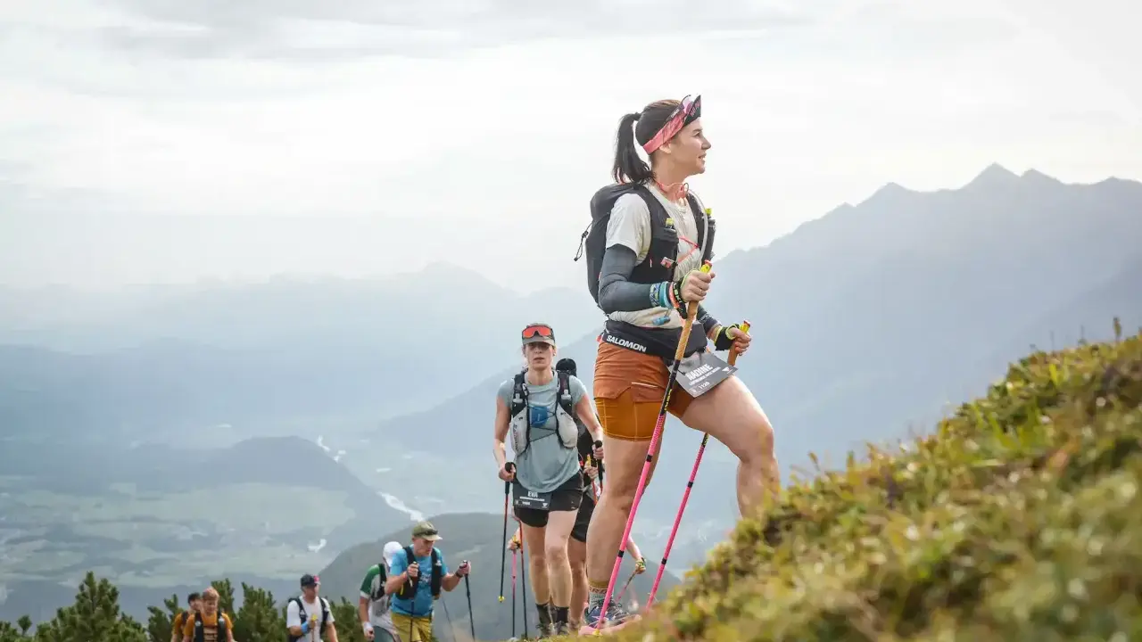 Läuferinnen und Läufer trainieren bergauf gehen in den Alpen. Sie nutzen Stöcke zur Unterstützung.