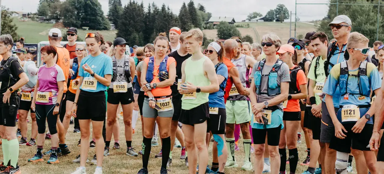 Läufer stehen bereit für den Lauf "3 Kings 3 Hills". Die Teilnehmenden tragen Startnummern und Laufbekleidung.