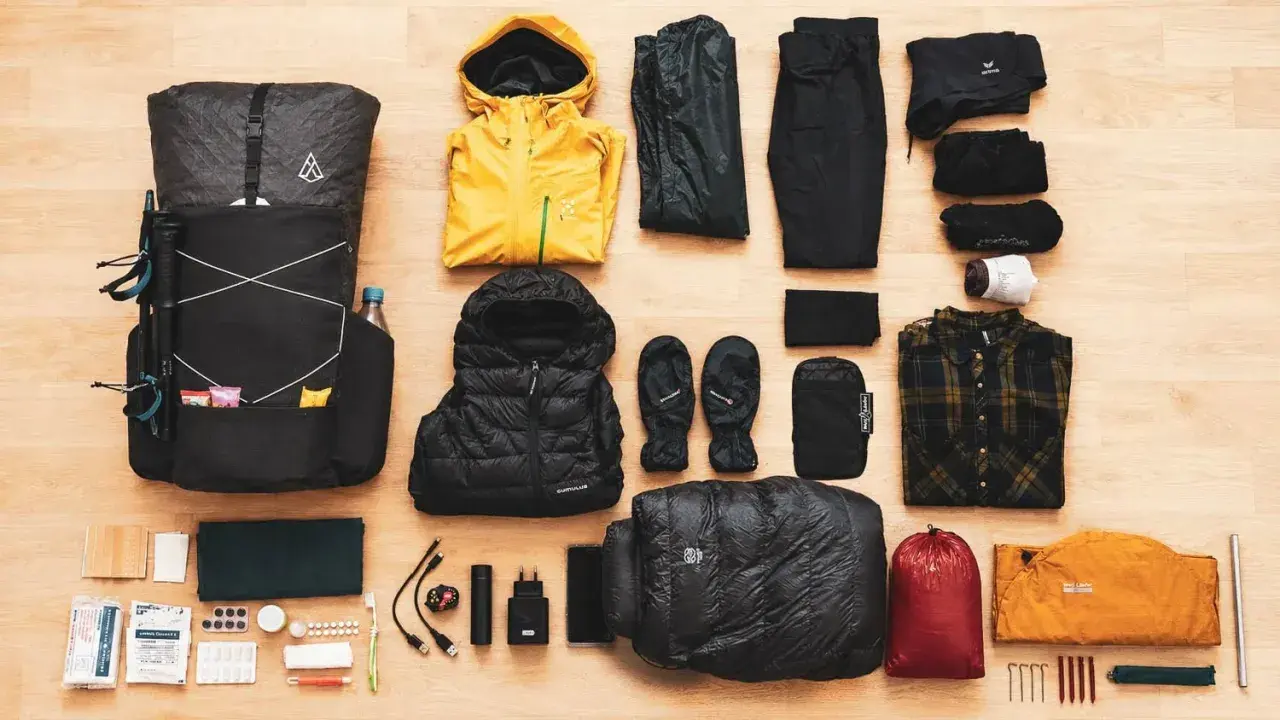 Rucksack, Wanderstöcke, gelbe Regenjacke, Daunenjacke, Handschuhe, Schlafsack, Zelt und Kleidung für **ultralight trekking**.