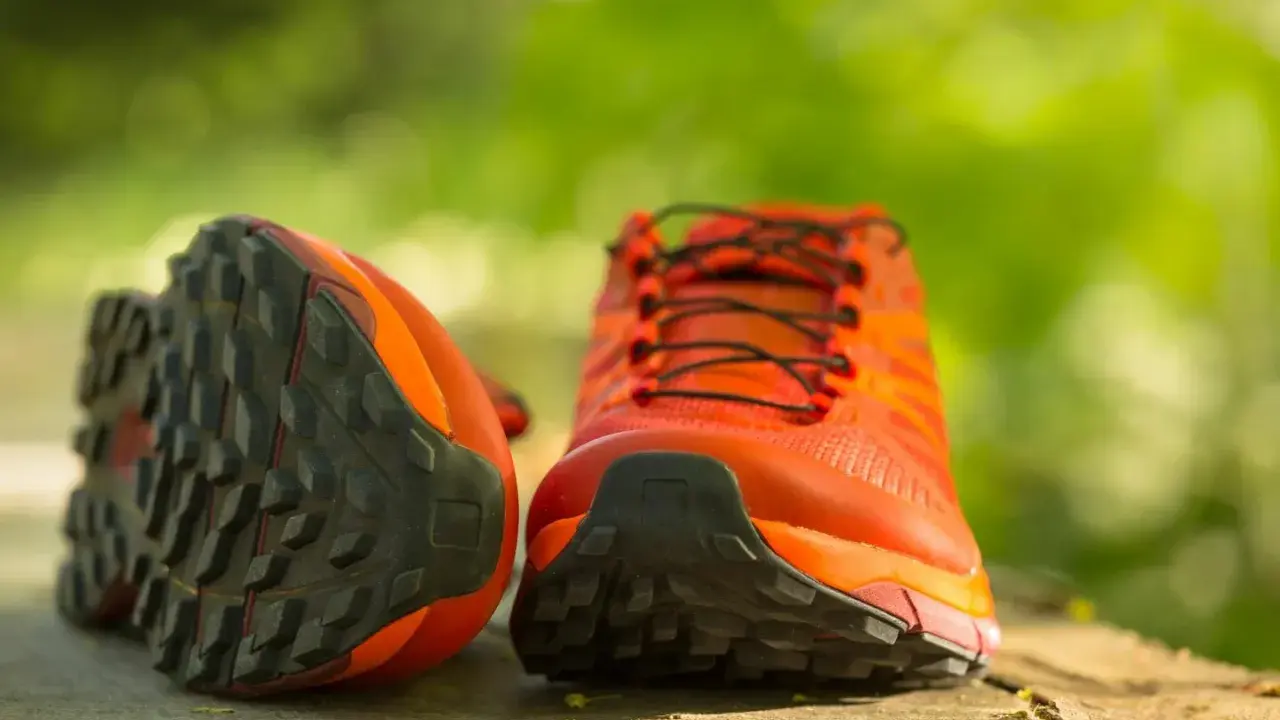 Leuchtend orange Trailrunning-Schuhe mit grobstolliger Sohle, bereit für neue Abenteuer. Perfekt, um bergschuhe neu besohlen zu lassen und wieder loszulegen.
