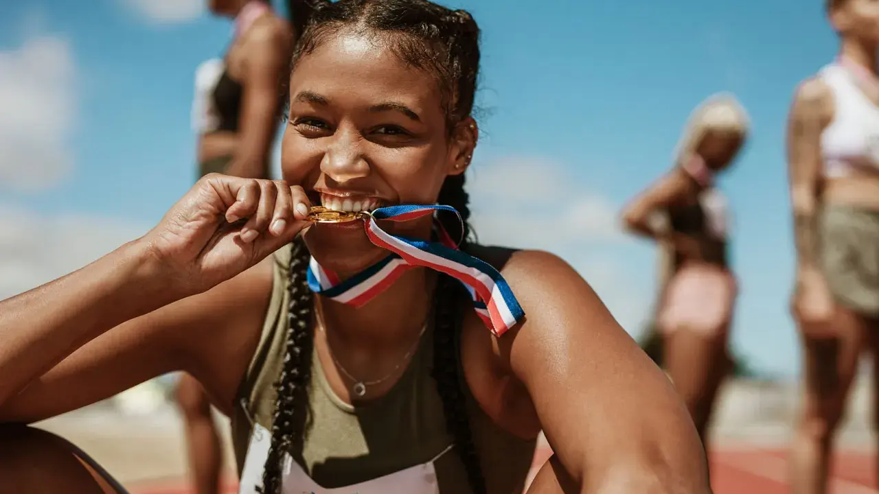 Läuferin beißt stolz in ihre Goldmedaille. Ihr Trainingsplan Laufen 10 km hat sich ausgezahlt.