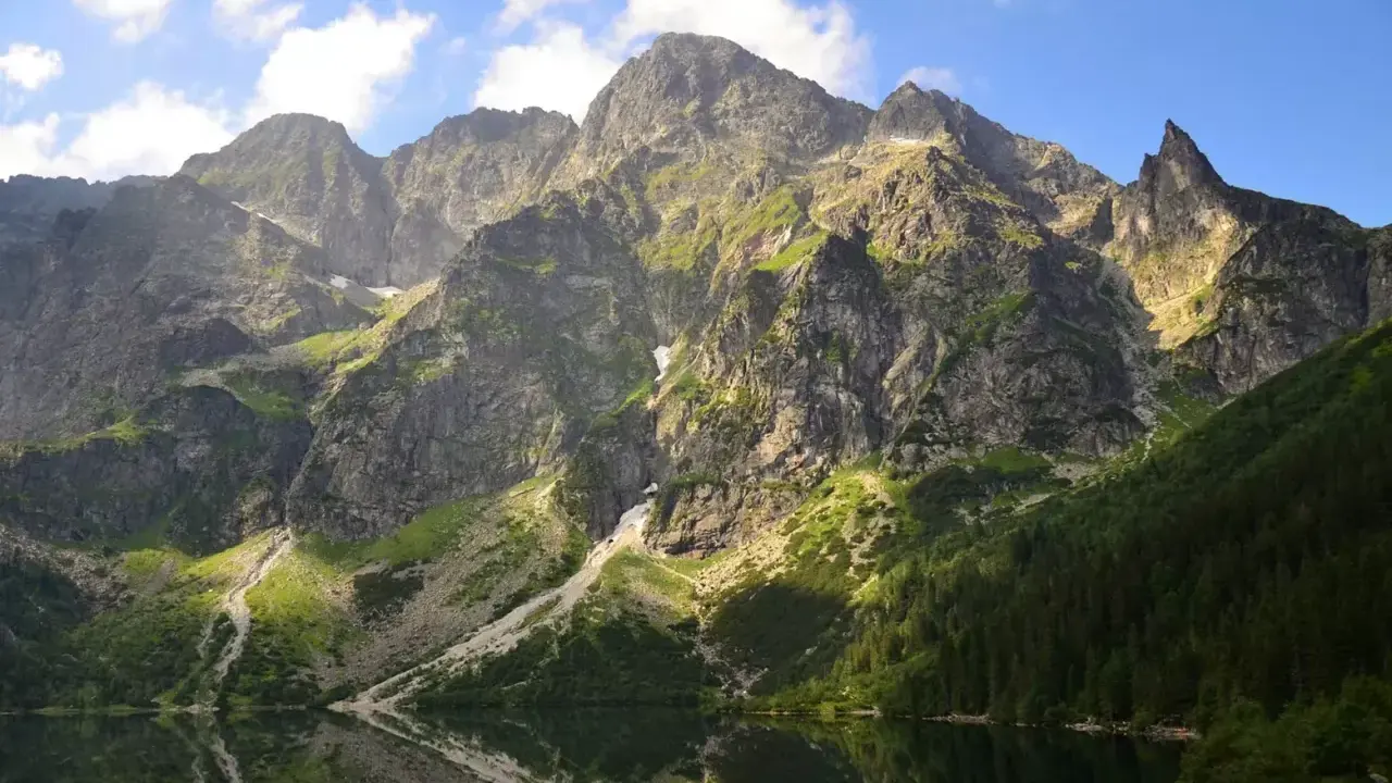Majestätische Berge im Tatra Gebirge laden zum Wandern ein. Ein ruhiger See spiegelt die felsigen Hänge und den blauen Himmel wider.