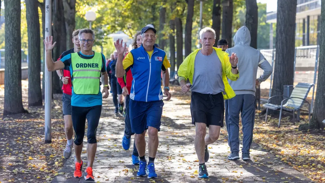 Herren genießen slow jogging im Herbstpark, einige winken fröhlich.