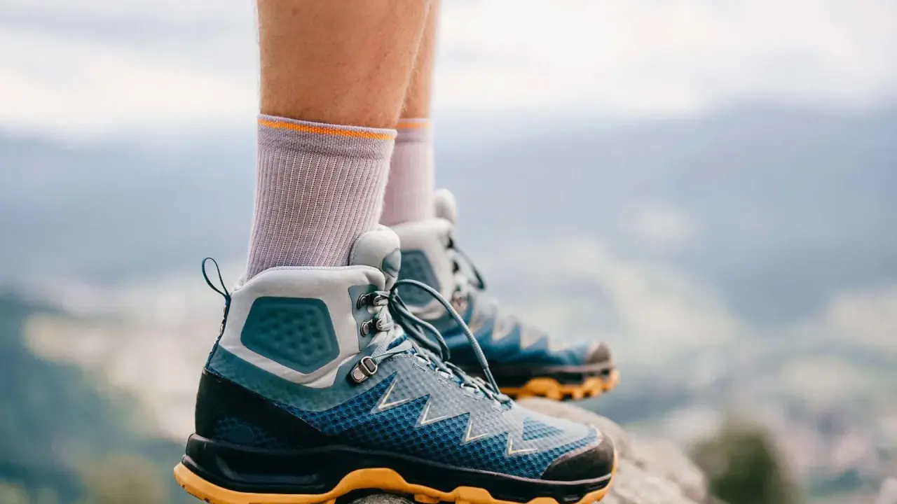 Graue Socken und blaue Wanderschuhe mit gelber Sohle stehen auf einem Felsen. Bereit für das nächste Abenteuer in den Bergen.
