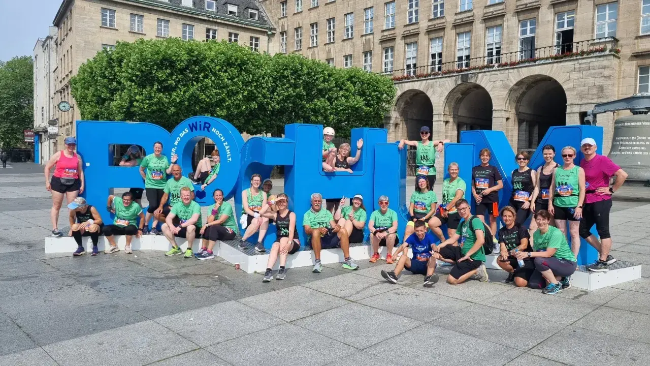Gruppe feiert Erfolg beim urban run Bochum vor riesiger blauer Schrift.