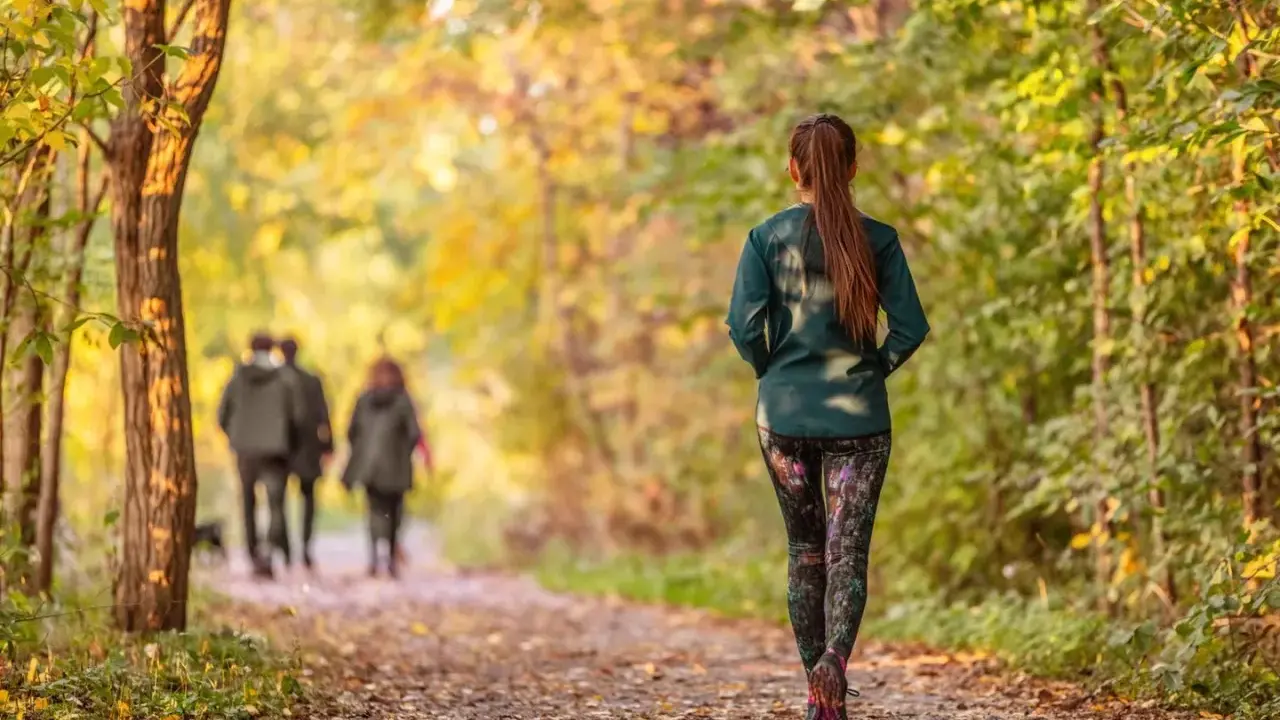 Frau im Herbstwald beim Power Walking, während im Hintergrund ein Paar spazieren geht.