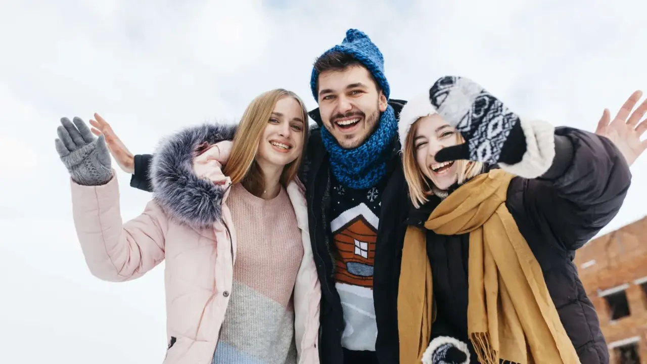Drei Freunde genießen das Wandern im Winter. Sie tragen warme Kleidung wie Daunenjacken, Mützen und Handschuhe.