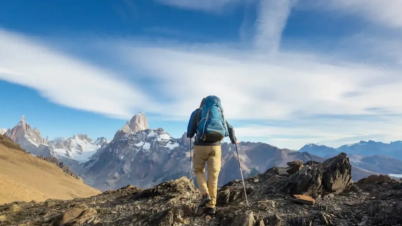 Ein Wanderer mit Rucksack und Stöcken erklimmt einen felsigen Grat. Die majestätische Bergkulisse zeigt die wahre trekking bedeutung: Abenteuer und Freiheit.