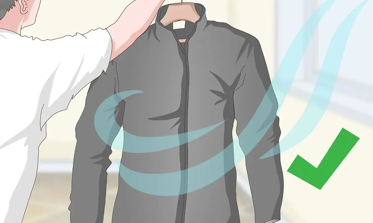 Eine graue Fleecejacke wird zum Trocknen aufgehängt. Blaue Wellen symbolisieren Luftzirkulation, ein grüner Haken zeigt Erfolg an. So wird die Fleecejacke gewaschen und getrocknet.