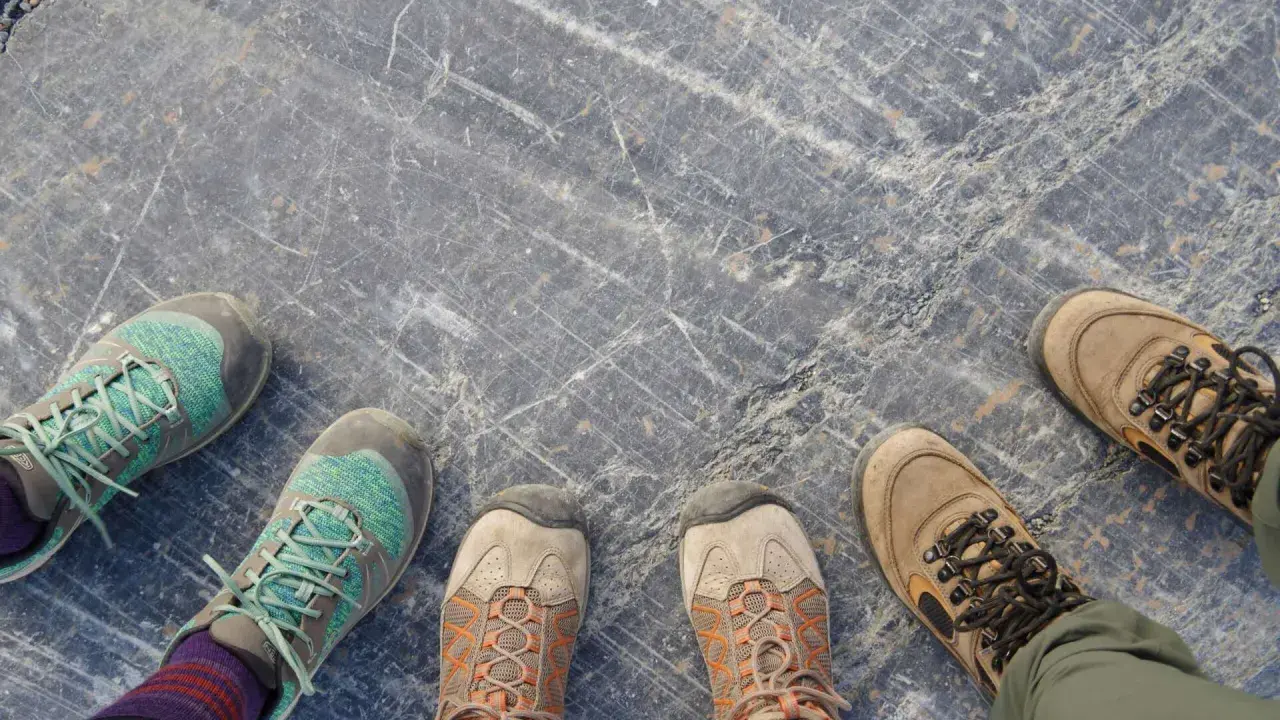 Vier Paar Wanderschuhe auf grauem Steinboden. Sie zeigen, wie sollten Wanderschuhe sitzen: bequem, aber fest.