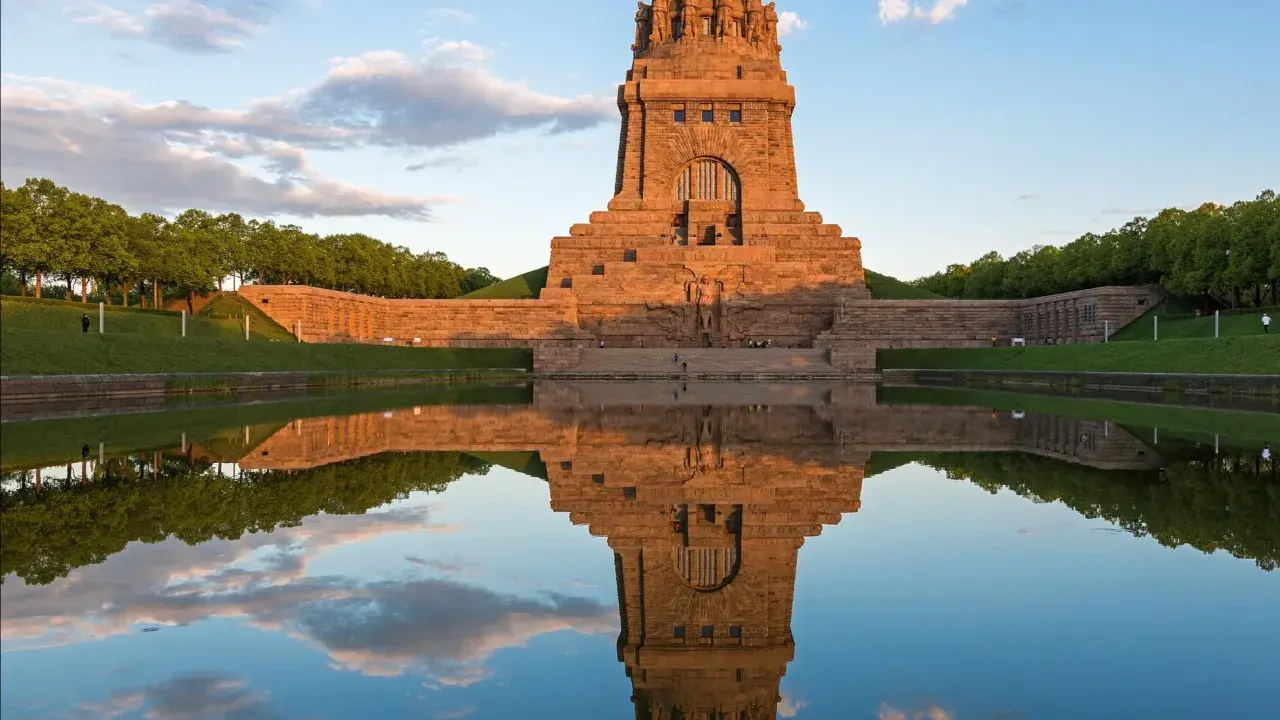Das Völkerschlachtdenkmal in Leipzig spiegelt sich im Wasser. Ein Läufer genießt die Abendstimmung.