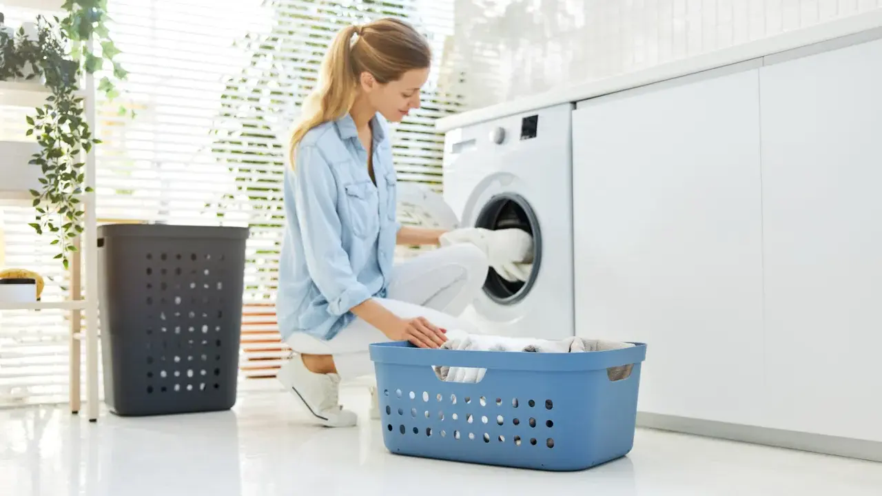 Frau lädt Wäsche in die Waschmaschine. So kann man eine Daunenjacke waschen ohne Trockner.
