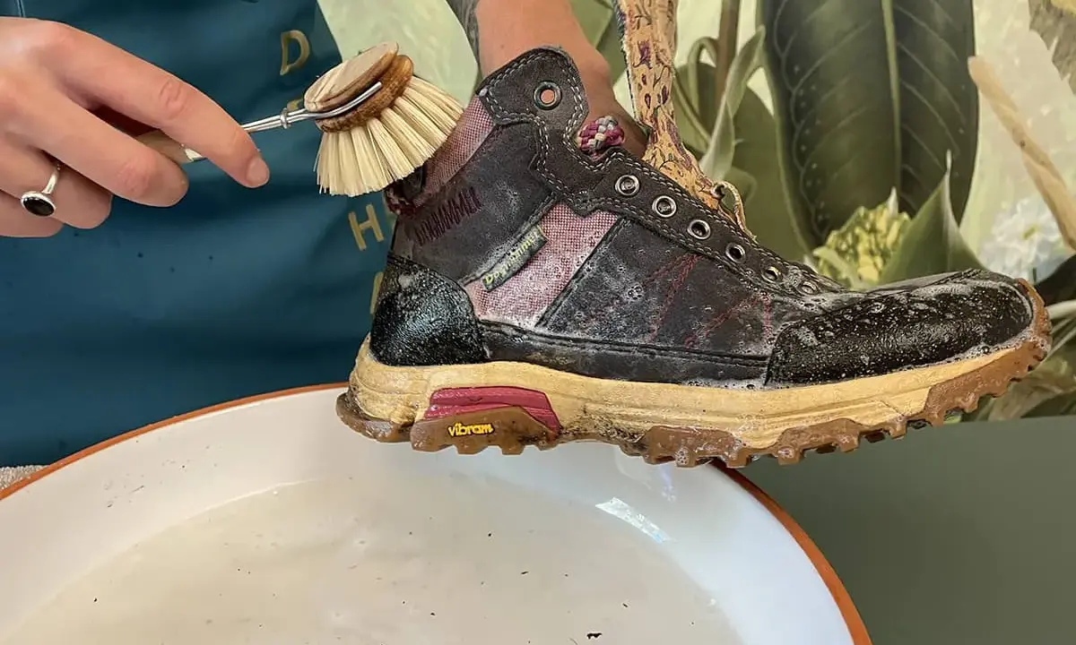Schuhbürste reinigt schmutzige Wanderschuhe in Seifenwasser. So pflegen Sie Ihre Wanderschuhe richtig.