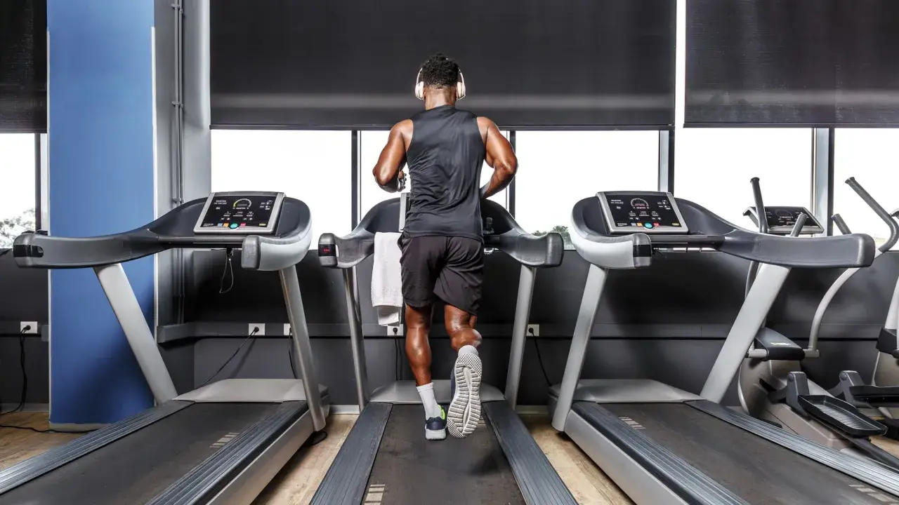 Mann mit Kopfhörern absolviert ein intensives Laufband Training im Fitnessstudio.