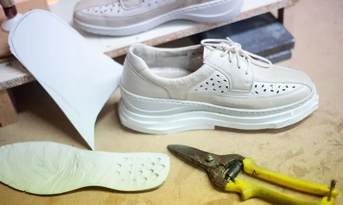 Schuhe mit Abrollsohle im Test: Ein Muster, eine Sohle und eine Schere liegen bereit.