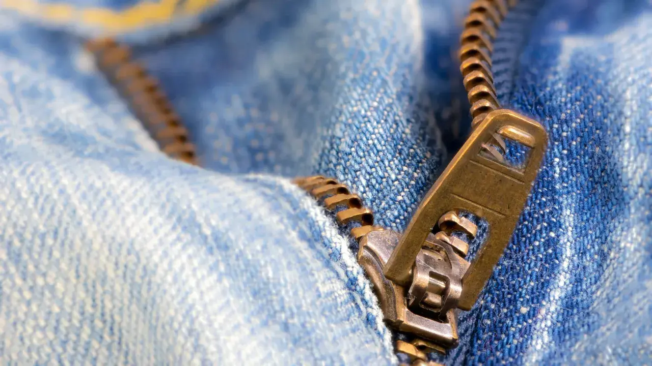 Nahaufnahme eines Reißverschlusses an Jeans. Der Schieber ist halb geöffnet. Ein guter Zeitpunkt, um den Reißverschluss reparieren zu lassen.