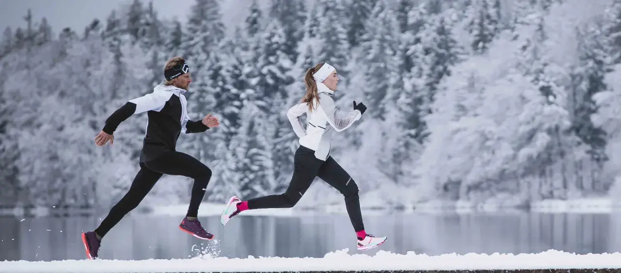 Zwei Läufer in warmer Winterkleidung genießen einen Lauf im Schnee.