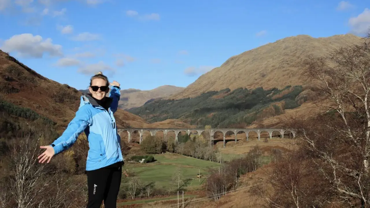 Glückliche Frau genießt das Wandern in Schottland vor einer beeindruckenden Brücke in den Highlands.