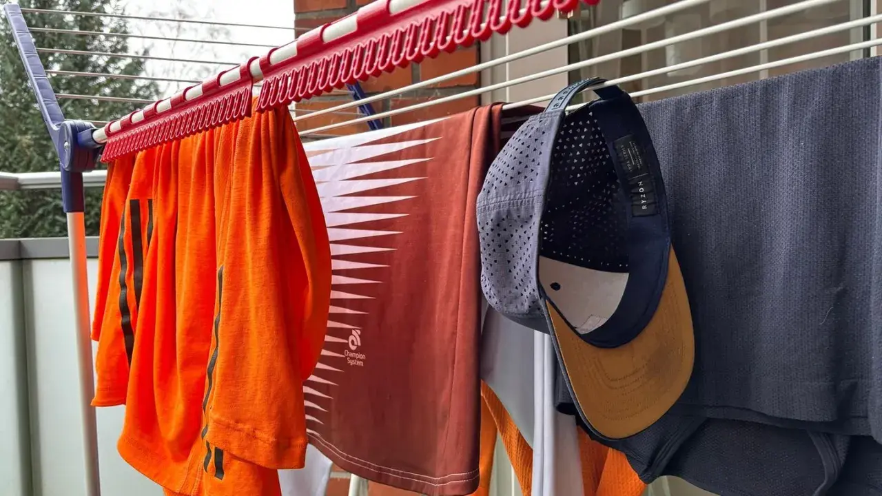 Wäscheleine mit Kleidung, darunter ein orangefarbenes Shirt, ein braunes Shirt und eine Kappe, die zum cap reinigen aufgehängt wurde.