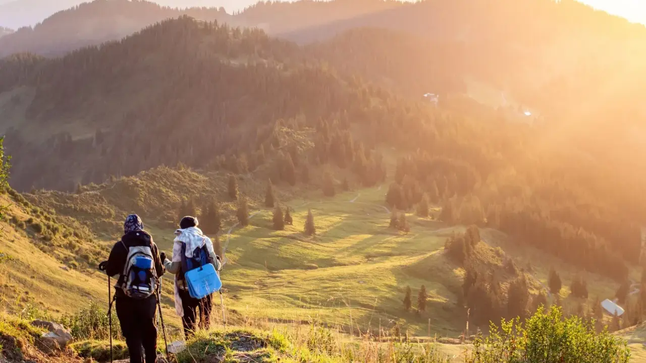 Zwei Wanderer genießen einen **great trail** in Kanada. Die Sonne taucht die bewaldeten Hügel in goldenes Licht.