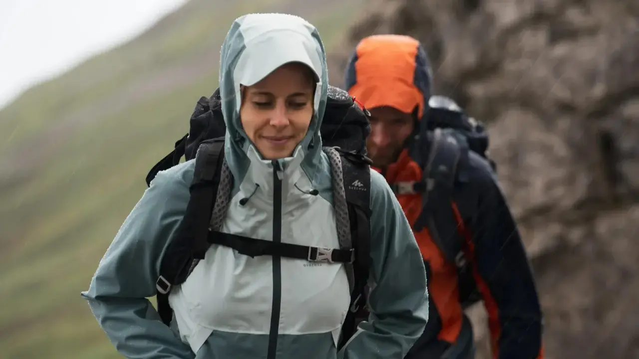 Zwei Wanderer im Regen. Die Frau trägt eine hellblaue Jacke, die perfekt ist, wenn man sich fragt, welche Jacke zum Wandern bei schlechtem Wetter am besten geeignet ist.