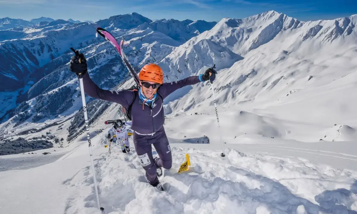 Ein Mann im orangefarbenen Helm jubelt beim Skyrunning in den verschneiten Alpen.