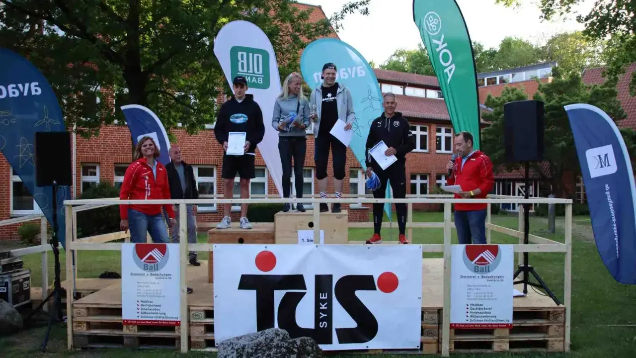 Siegerehrung beim Hachelauf Syke: Läufer auf dem Podium, Moderation und Sponsoren-Banner im Hintergrund.