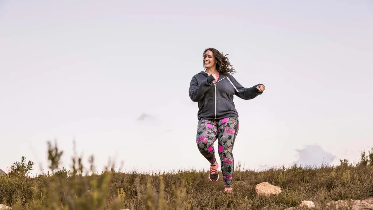 Frau joggt mit Gewichten in bunter Hose durch die Natur.