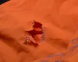 Ein Loch in einer orangefarbenen Polyesterjacke, bereit für einen Flicken.