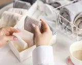 Hände sortieren gefaltete Socken in einer Schubladenteilung. Nach dem Wandersocken waschen ist Ordnung angesagt.
