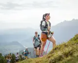 Läuferinnen und Läufer trainieren bergauf gehen in den Alpen. Sie nutzen Stöcke zur Unterstützung.