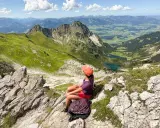 Ein Mädchen mit Rucksack genießt die Aussicht auf die Berge bei Oberstdorf. Ein leichtes Wandern mit toller Belohnung.