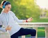 Frau mit Kopfhörern und Handy-Armband spielt Luftgitarre beim Joggen. Die Musik zum Joggen macht sie glücklich.