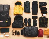 Rucksack, Wanderstöcke, gelbe Regenjacke, Daunenjacke, Handschuhe, Schlafsack, Zelt und Kleidung für **ultralight trekking**.