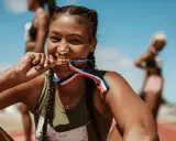 Läuferin beißt stolz in ihre Goldmedaille. Ihr Trainingsplan Laufen 10 km hat sich ausgezahlt.