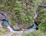 Türkisblaues Wasser rauscht durch eine enge Schlucht mit steilen Felswänden, bewachsen mit üppigem Grün. Eine Holzbrücke führt über die Klammen in Bayern.