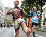Mann mit schmutzigen Füßen jubelt nach einem Halbmarathon ohne Training. Er hält eine Medaille hoch und gibt Daumen hoch.