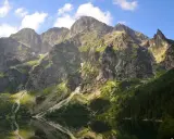 Majestätische Berge im Tatra Gebirge laden zum Wandern ein. Ein ruhiger See spiegelt die felsigen Hänge und den blauen Himmel wider.