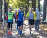 Herren genießen slow jogging im Herbstpark, einige winken fröhlich.