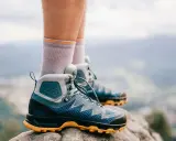 Graue Socken und blaue Wanderschuhe mit gelber Sohle stehen auf einem Felsen. Bereit für das nächste Abenteuer in den Bergen.