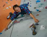 Frau klettert an einer Boulderwand. Sie trägt ein kariertes Hemd und bequeme Kleidung, ideal, was man zum Bouldern anzieht.