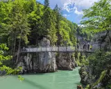 Menschen überqueren eine Hängebrücke während einer entenlochklamm wanderung. Türkises Wasser fließt unter der Brücke hindurch, umgeben von steilen Felswänden und üppigem Grün.