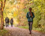 Frau im Herbstwald beim Power Walking, während im Hintergrund ein Paar spazieren geht.