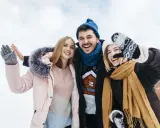 Drei Freunde genießen das Wandern im Winter. Sie tragen warme Kleidung wie Daunenjacken, Mützen und Handschuhe.
