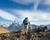 Ein Wanderer mit Rucksack und Stöcken erklimmt einen felsigen Grat. Die majestätische Bergkulisse zeigt die wahre trekking bedeutung: Abenteuer und Freiheit.