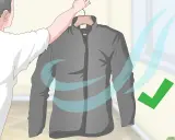 Eine graue Fleecejacke wird zum Trocknen aufgehängt. Blaue Wellen symbolisieren Luftzirkulation, ein grüner Haken zeigt Erfolg an. So wird die Fleecejacke gewaschen und getrocknet.