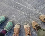 Vier Paar Wanderschuhe auf grauem Steinboden. Sie zeigen, wie sollten Wanderschuhe sitzen: bequem, aber fest.