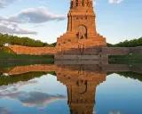 Das Völkerschlachtdenkmal in Leipzig spiegelt sich im Wasser. Ein Läufer genießt die Abendstimmung.